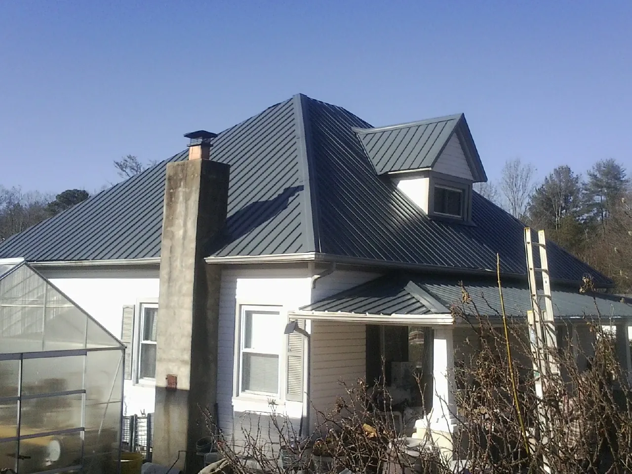 Dark blue standing seam metal roof on a white farmhouse with dormer — Slate & Tile Roof Repair by Roofing Brothers in Huntsburg