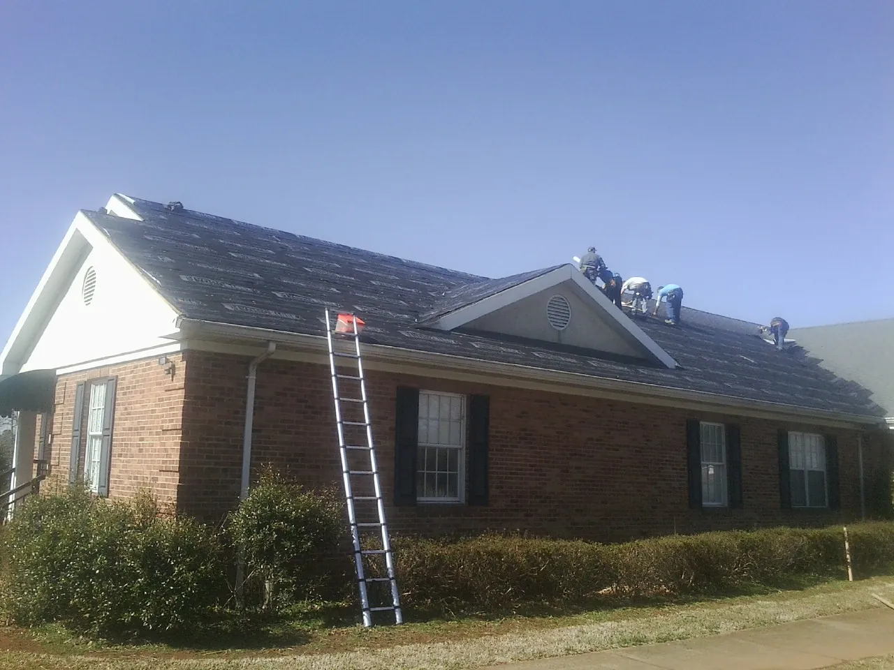 Crew tearing shingles off a brick ranch roof with a ladder set — Emergency Roof Repair work by our crew in Huntsburg