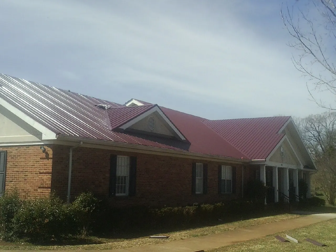 Red metal roof with gabled entries on a long brick building, from a Hail Damage Roof Repair job in Huntsburg