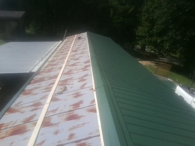 Old rusted panels beside newly installed green metal roofing — Wind Damage Roof Repair by Roofing Brothers in Huntsburg