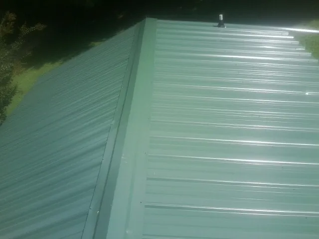 New green metal panels meeting at the ridge of a roof — Flat Roof Repair work by our crew in Huntsburg