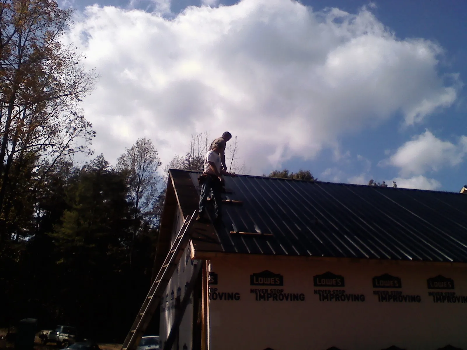 Roofer fastening dark metal panels high against a cloudy sky, from a Roof Inspection job in Huntsburg
