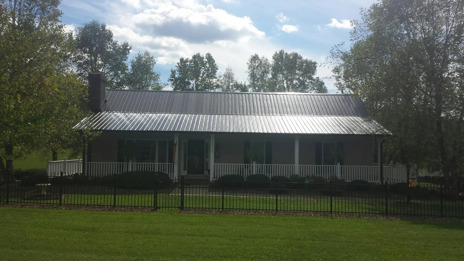 Gray metal roof on a brick ranch with a full width front porch — Gutter Guard Installation work by our crew in Huntsburg