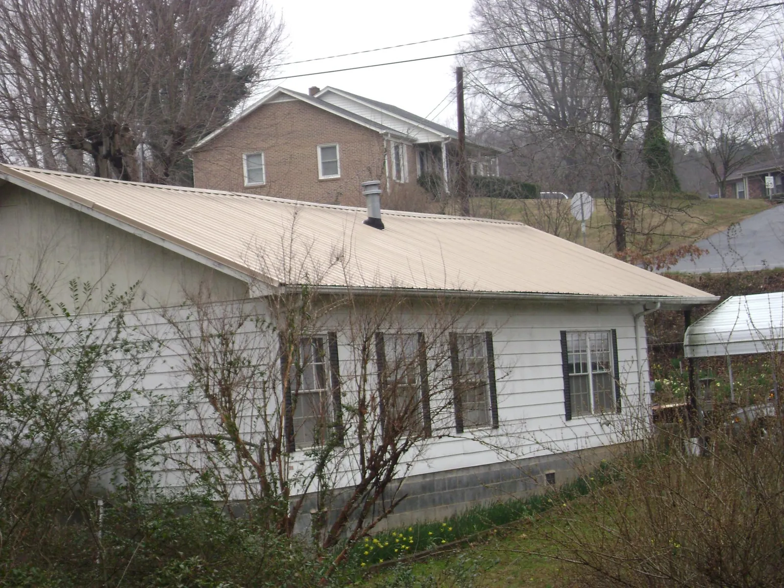 Tan metal roof on a white sided house set into a hillside — Commercial Roofing by Roofing Brothers in Huntsburg