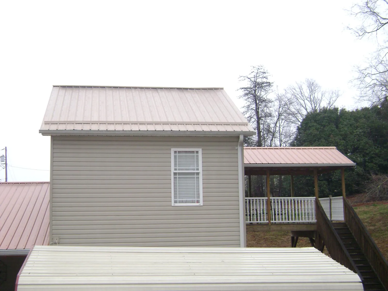 Tan metal roofs on a two story addition and attached porch, from a Roof Replacement job in Huntsburg
